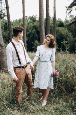 Tarz sahibi genç bir çift, kızın elini tutan, gülümseyen ve birbirine bakan bir erkek.