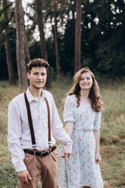 Tarz sahibi genç bir çift, erkek kıza sarılıyor, yeşil bahar ormanlarında gülümsüyor.