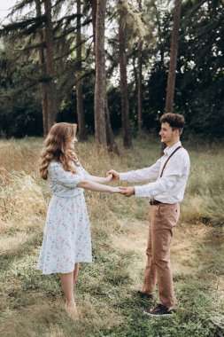 Tarz sahibi genç bir çift, erkek kıza sarılıyor, yeşil bahar ormanlarında gülümsüyor.