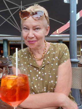 Portrait of an attractive mature woman with a glass of Aperol-Spritz on the table in front of her