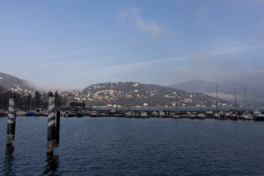 COMO, İtalya - 25 Şubat 2023: rıhtımdan Como Gölü manzarası. Sabahları, sisli dağlarda