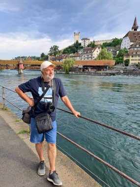 İsviçre 'nin Lucerne şehrindeki Reuss nehrinin setinde kameralı olgun bir adam.