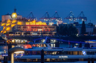 HAMBURG, Almanya - 15 AĞUSTOS 2024 Hamburg Limanı 'nda akşam. Ön planda aydınlatılmış gemiler, arka planda ise Aslan Kral müzikalinin sahnelendiği tiyatrolar var.