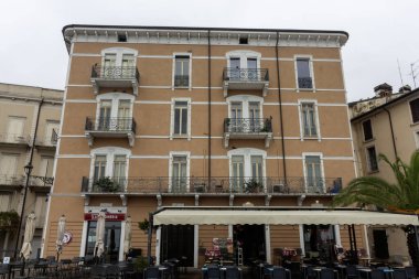 DESENZANO DEL GARDA, İTALYA - 25 Ekim 2024: Desenzano del Garda 'da birden fazla kat, balkon ve zemin kattaki tenteli ve açık hava oturma yerleri olan geleneksel bir İtalyan binasının manzarası