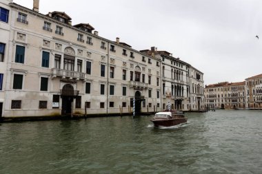 Venedik, İtalya - 24 Ekim 2024 Venedik, İtalya 'da tarihi binaların rıhtımda yüzdüğü ve çeşitli teknelerin su yolunda yüzdüğü manzaralı bir kanal manzarası. Bulutlu gökyüzü