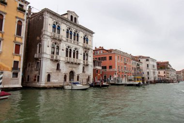 Venedik, İtalya - 24 Ekim 2024: rengarenk tarihi binaları ve liman boyunca demirlemiş gondolları olan Venedik kanalı manzarası. Bulutlu gökyüzü