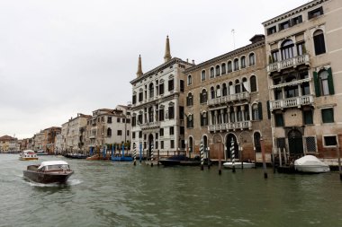 Venedik, İtalya - 24 Ekim 2024 Venedik, İtalya 'da tarihi binaların rıhtımda yüzdüğü ve çeşitli teknelerin su yolunda yüzdüğü manzaralı bir kanal manzarası. Bulutlu gökyüzü