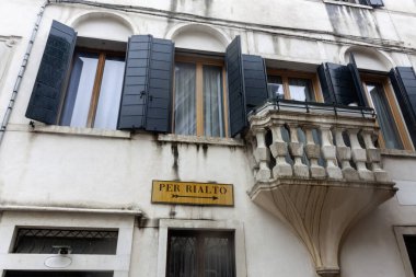 Venedik, İtalya 'da taş balkonu ve pencereleri kepenkleri olan bir binada' Per Rialto '(Rialto' ya doğru) yönlü bir işaret.