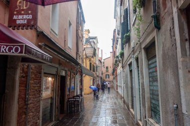 VENICE, İtalya - 24 Ekim 2024: Venedik, İtalya 'da dar bir hat (sokak), 2024 Ekim ayı sonunda, insanların yağmurda şemsiyelerle yürüdüğü