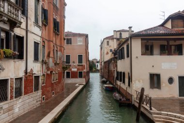 İtalya, Venedik 'te, suyun üzerindeki renkli binaların yansımalarının olduğu dar bir kanal manzarası. Kanal kıyılarına demirlemiş birkaç küçük tekne var.