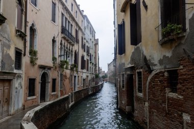 İtalya, Venedik 'te, suyun üzerindeki renkli binaların yansımalarının olduğu dar bir kanal manzarası. Kanal kıyılarına demirlemiş birkaç küçük tekne var.