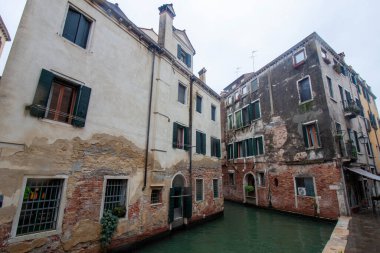 İtalya, Venedik 'te, suyun üzerindeki renkli binaların yansımalarının olduğu dar bir kanal manzarası. Kanal kıyılarına demirlemiş birkaç küçük tekne var.