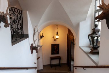 MEERSBURG, GERMANY - DECEMBER 7, 2024: Interior of Meersburg Castle, Germany, featuring arched ceilings, white walls, hunting trophies, a painting, and a hanging lamp in a hallway or near a staircase clipart