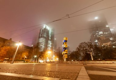 FRANKFURT (MAIN), GERMANY - DECEMBER 1, 2024: The Euro sign sculpture on Willy-Brandt-Platz at night in Frankfurt, Germany, with skyscrapers in fog in the background clipart