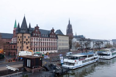 FRANKFURT (MAIN), GERMANY - DECEMBER 2, 2024: View of the Museumsufer (Museum Embankment) in Frankfurt am Main, Germany, with historic buildings and docked river boats on a cloudy day clipart