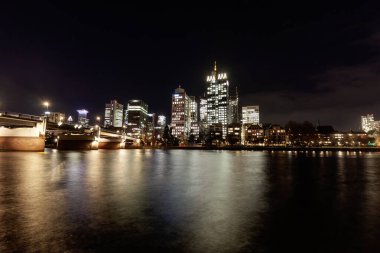 FRANKFURT (MAIN), GERMANY - 3 Aralık 2024: Frankfurt am Main Skyline, Bankenviertel 'deki modern gökdelenlerin ışıklarını ve ön plandaki bir köprüyü yansıtan bir gece görüntüsü
