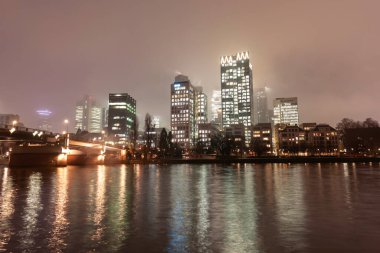 FRANKFURT, Almanya - 2 ARALIK. 2024: Geceleri aydınlık gökdelenleri, köprüsü ve nehri olan modern şehir manzarası