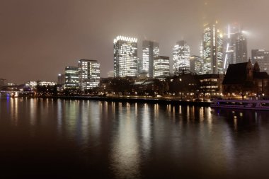 FRANKFURT, Almanya - 2 ARALIK. 2024: Aydınlatılmış binaları, köprüsü ve dönme dolabı olan şehir manzarası