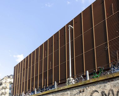 Yatay kirişleri ve endüstriyel estetiğiyle bina belirgin bir şekilde açık mavi gökyüzüne karşı sergileniyor. Strasbourg