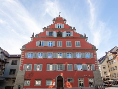 LINDAU, GERMANY - 22 Mart 2025: Lindau, Almanya 'da Neue Rathaus (Yeni Şehir Salonu)' nun çarpıcı kırmızı cephesinin alçak açılı bir görüntüsü, parlak mavi bulutlu bir gökyüzü altında