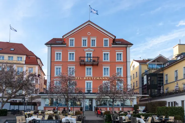 LINDAU, GERMANY - 22 Mart 2025: Bu görüntü, Lindau, Almanya 'da yer alan beyaz pencere çerçeveli önemli bir somon rengi bina olan Reutemann Oteli' nin cephesini gösteriyor
