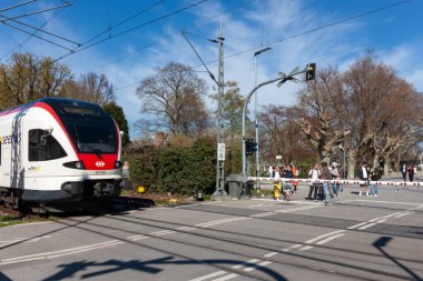 KONSTANZ, GERMANY - 5 Nisan 2025: Almanya 'nın Konstanz kentindeki bir geçitte beyaz ve kırmızı renkli modern bir tren görülüyor