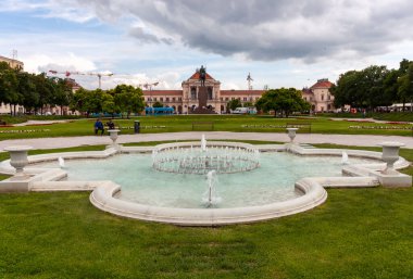 ZAGREB, CROATIA - 22 Mayıs 2025: Hırvatistan 'ın Zagreb kentinde ortasında köpüklü su püskürtüleri bulunan dekoratif bir beyaz taş çeşmenin yer aldığı pitoresk bir park sahnesi