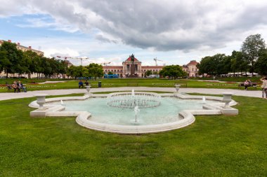 ZAGREB, CROATIA - 22 Mayıs 2025: Hırvatistan 'ın Zagreb kentinde ortasında köpüklü su püskürtüleri bulunan dekoratif bir beyaz taş çeşmenin yer aldığı pitoresk bir park sahnesi