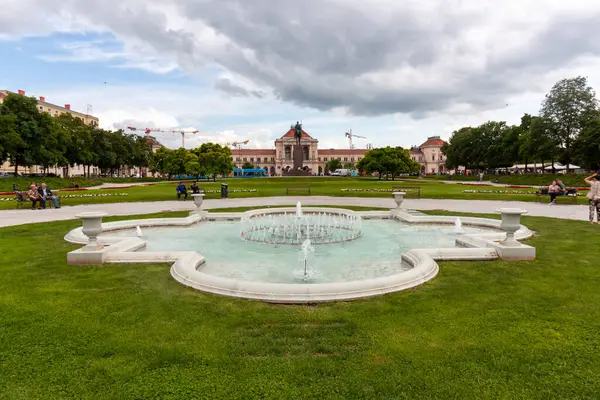 ZAGREB, CROATIA - 22 Mayıs 2025: Hırvatistan 'ın Zagreb kentinde ortasında köpüklü su püskürtüleri bulunan dekoratif bir beyaz taş çeşmenin yer aldığı pitoresk bir park sahnesi