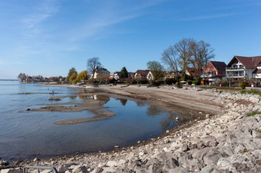 Almanya 'nın Langenargen kentindeki Constance Gölü' ndeki (Bodensee) alçak su seviyelerinin geniş ve sakin bir görüntüsü, açık ve güneşli bir günde kumlu ve çakıllı bir kıyı şeridini gözler önüne serer.