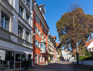 LINDAU, GERMANY - 26 HAZİRAN 2025: Almanya 'nın tarihi eski Lindau kasabasında bir dizi geleneksel Avrupa binalarının berrak, parlak mavi gökyüzü altında sergilendiği büyüleyici bir sokak sahnesi
