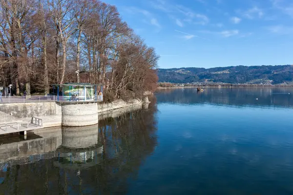Almanya 'nın Lindau kentinden gelen sakin bir kış veya ilkbahar manzarası, su üzerinde uzanan modern, dairesel bir pavyon yapısını gözler önüne seriyor.