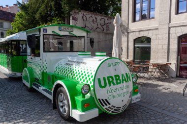 LJUBLJANA, SLOVENIA - 18 Mayıs 2025: Parlak gün ışığı altında Slovenya 'nın Ljubljana kentindeki kaldırım taşı sokağında eşsiz yeşil ve beyaz bir turist treni yakalayan büyüleyici bir sokak manzarası