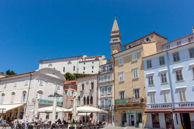 PİRAN, SLOVENIA - 19 Mayıs 2025: Piran, Slovenya 'daki hareketli Tartini Meydanı' nın canlı, güneşli manzarası, açık mavi gökyüzü altında ikonik simgelerini sergiliyor