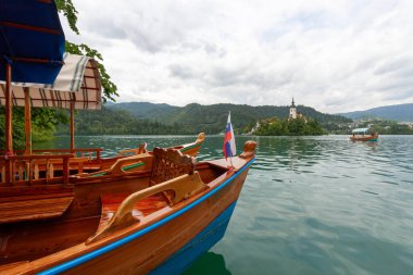 Slovenya 'nın Bled Gölü' nün sakin, yeşil-mavi sularına demirlemiş iki geleneksel ahşap pletna teknesi var. Teknenin ön tarafında belirgin bir şekilde küçük bir Slovenya bayrağı sergileniyor