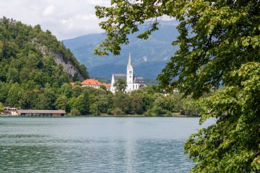 Bled Gölü 'nün sakin suları boyunca manzaralı bir manzara, yemyeşil tepelerin eteklerindeki büyüleyici Bled kasabasını gözler önüne seriyor. Belirgin bir şekilde St. Martin Kilisesi 'nin çan kulesi sergilenmektedir.