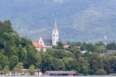 Bled Gölü 'nün sakin suları boyunca manzaralı bir manzara, yemyeşil tepelerin eteklerindeki büyüleyici Bled kasabasını gözler önüne seriyor. Belirgin bir şekilde St. Martin Kilisesi 'nin çan kulesi sergilenmektedir.