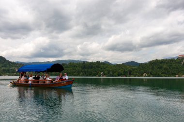 BLED, SLOVENIA - 20 Mayıs 2025: Ayırt edici mavi bir gölgelikle kaplı geleneksel ahşap pletna tekne, Slovenya 'nın Bled Gölü' nün yeşil renkli sularında süzülüyor