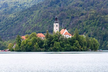Slovenya, Bled Gölü 'nün sakin ve geniş bir görüntüsü. Ortasında ikonik Bled Adası yer alıyor. Meryem 'in Hacı Kilisesi, belirgin beyaz ve kırmızı çatılı mimarisi ve uzun kulesi ile