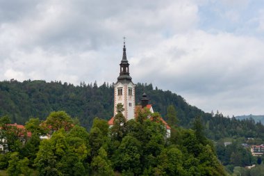 Slovenya 'nın Bled Gölü' nün ortasındaki yemyeşil ağaçların üzerinde yükselen, Bled Adası 'ndaki Meryem' in Varsayımının ikonik hac kilisesinin huzurlu bir manzarası.