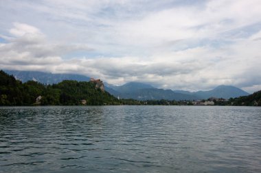 Bled Gölü 'nün pitoresk manzarası ön plandaki yemyeşil yapraklar tarafından çerçevelenmiş ve turkuaz sulara kısa bir bakış sunuluyor. Slovenya