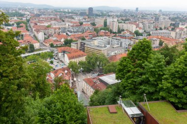 Geniş bir yükseltilmiş manzara, bulutlu bir günde Slovenya 'nın Ljubljana kentinin manzarasını yakalıyor. Kırmızı kiremitli çatılar ön plana hükmediyor ve eski kasabanın büyüleyici tarihi mimarisini gözler önüne seriyor.