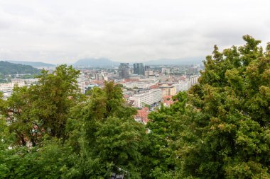 Geniş bir yükseltilmiş manzara, bulutlu bir günde Slovenya 'nın Ljubljana kentinin manzarasını yakalıyor. Kırmızı kiremitli çatılar ön plana hükmediyor ve eski kasabanın büyüleyici tarihi mimarisini gözler önüne seriyor.