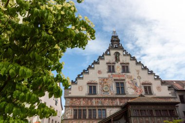 Almanya 'nın Lindau kentindeki tarihi Old Town Hall' u (Altes Rathaus), yemyeşil yaprakların ve beyaz çiçek kümelerinin ön planında büyüleyici bir alçak açı çekimi çerçeveler.