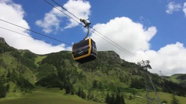 OBERSTDORF, GERMANY - 17 Temmuz 2025: Bavyera Alpleri 'nin yemyeşil yamaçlarına zarif bir şekilde inen siyah ve sarı renkli, modern bir teleferik gondolunun videosu.