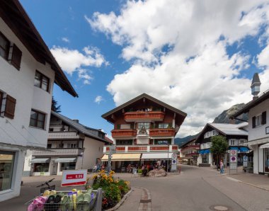 OBERSTDORF, ALMANY - 17 Temmuz 2025: Parlak, parçalı bulutlu bir gökyüzü altında geleneksel Bavyera mimarisinin sergilendiği Oberstdorf, Almanya 'da canlı bir sokak sahnesi