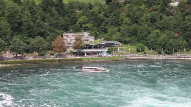 İnsanlarla dolu bir turist teknesi Ren Şelalesi yakınlarındaki çalkantılı, turkuaz sularda yol alır.