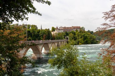 NEUHAUSEN AM RHEINFall, SWitzERLAND - 6 AĞUSTOS 2025: Ren nehrinin karşısındaki Ren Nehri 'nin en büyük şelalesine yakın demiryolu köprüsü. Schaffhausen ve Winterthur 'u birbirine bağlar