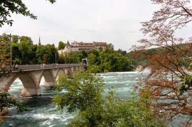 NEUHAUSEN AM RHEINFall, SWitzERLAND - 6 AĞUSTOS 2025: Ren nehrinin karşısındaki Ren Nehri 'nin en büyük şelalesine yakın demiryolu köprüsü. Schaffhausen ve Winterthur 'u birbirine bağlar