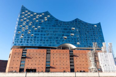 HAMBURG, GERMANY - 12 AĞUSTOS 2024: Hamburg 'daki sembolik Elbphilharmonie konser salonunun düşük açılı görüntüsü, etkileyici cam cephesini ve tuğla taban görüntüsünü gözler önüne seriyor